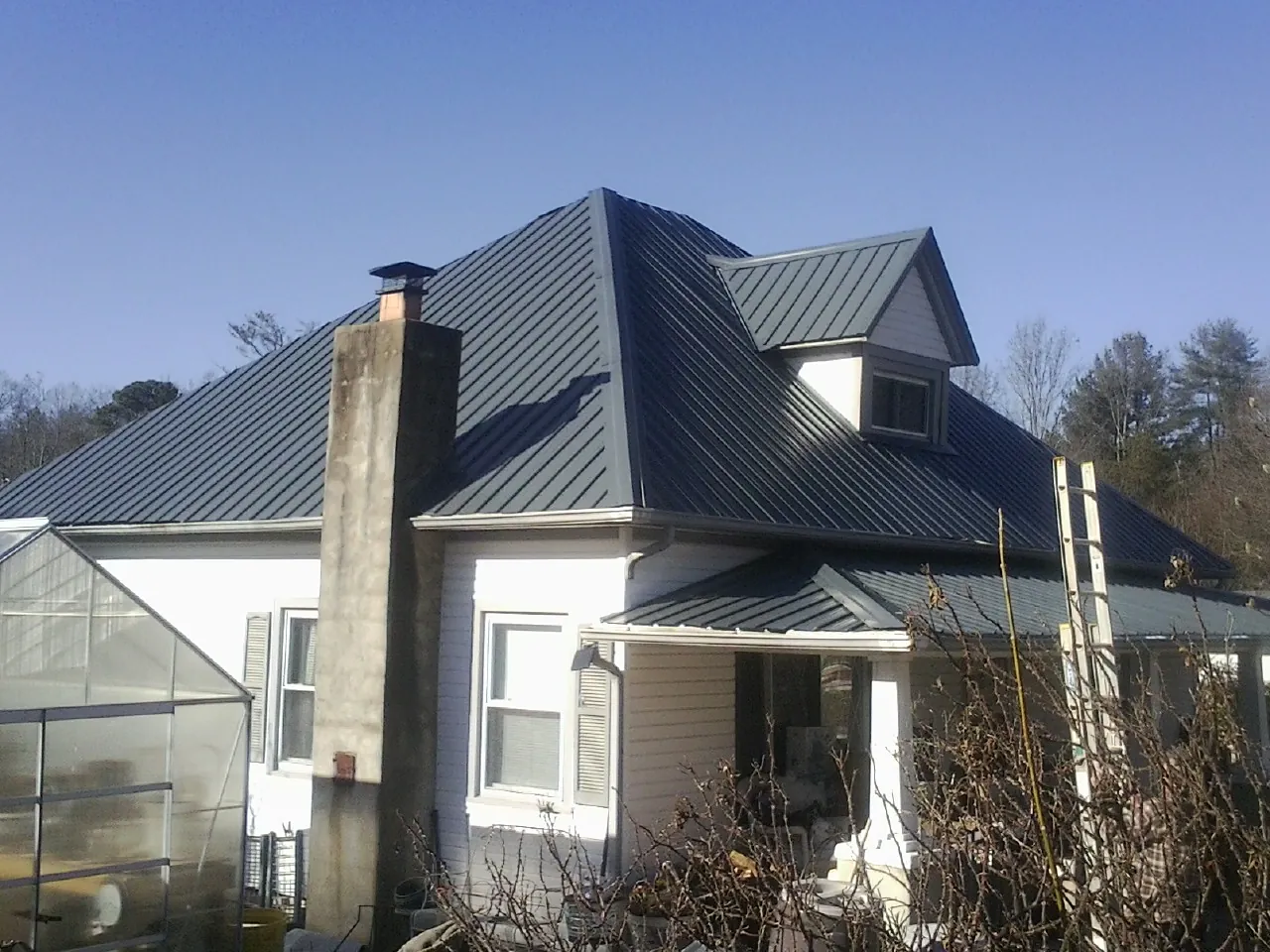 Dark blue standing seam metal roof on a white farmhouse with dormer — Slate & Tile Roof Repair by Roofing Brothers in Jeanerette