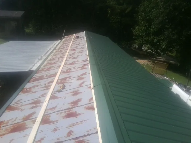 Old rusted panels beside newly installed green metal roofing — Wind Damage Roof Repair by Roofing Brothers in Jeanerette