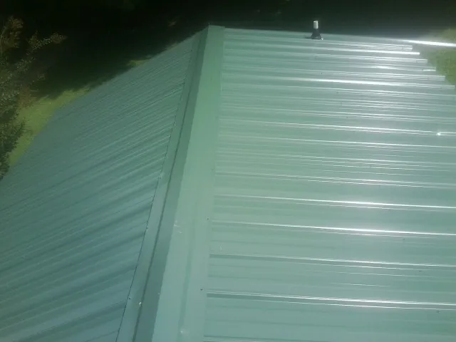 New green metal panels meeting at the ridge of a roof — Flat Roof Repair work by our crew in Jeanerette