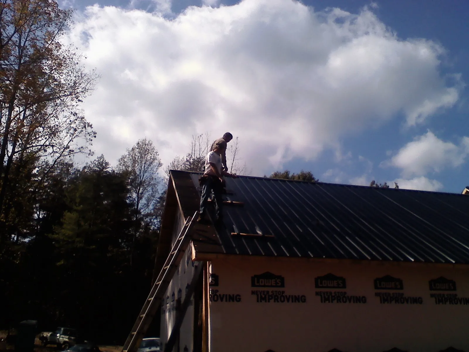 Roofer fastening dark metal panels high against a cloudy sky, from a Roof Inspection job in Jeanerette