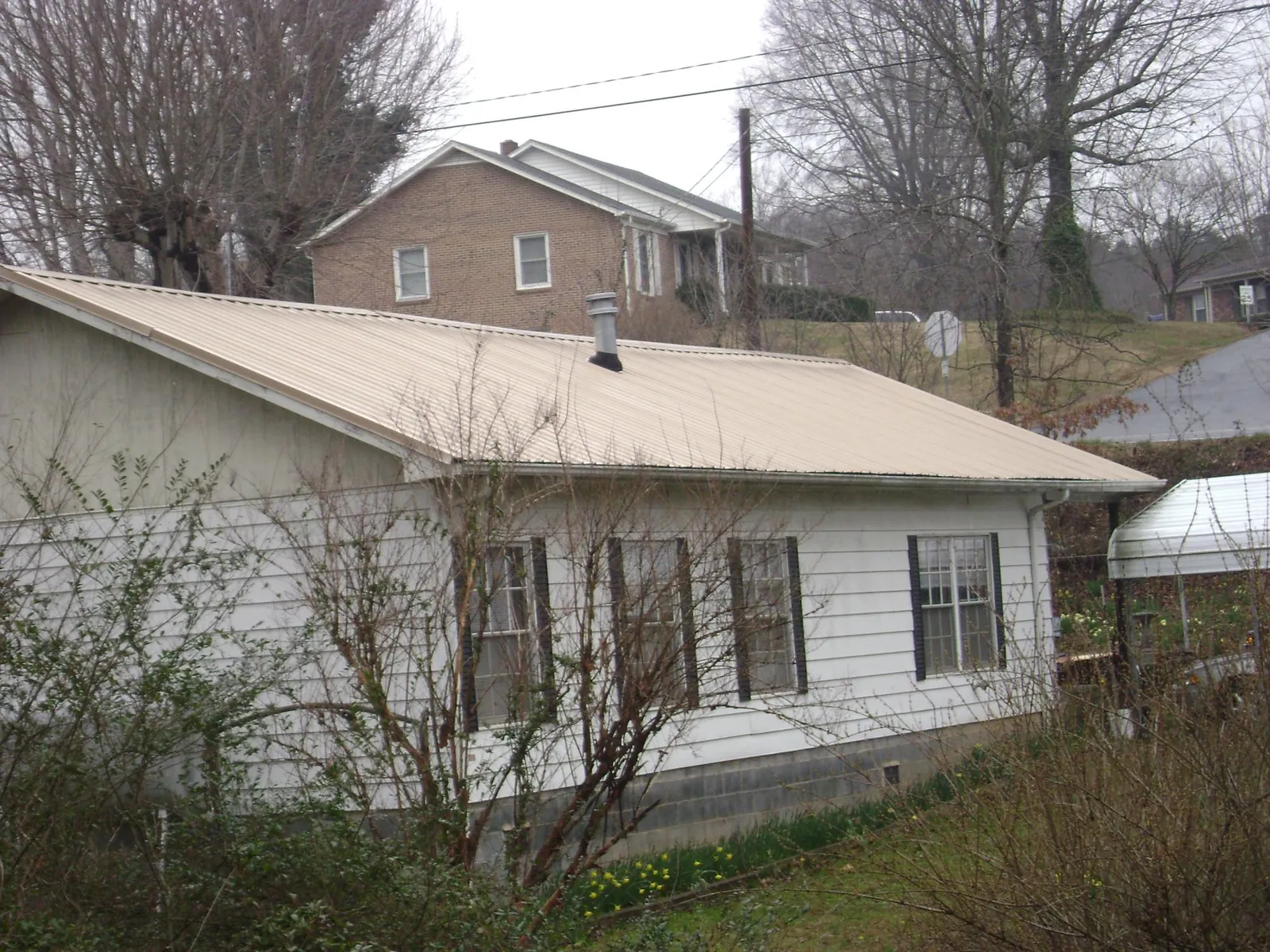 Tan metal roof on a white sided house set into a hillside — Commercial Roofing by Roofing Brothers in Jeanerette