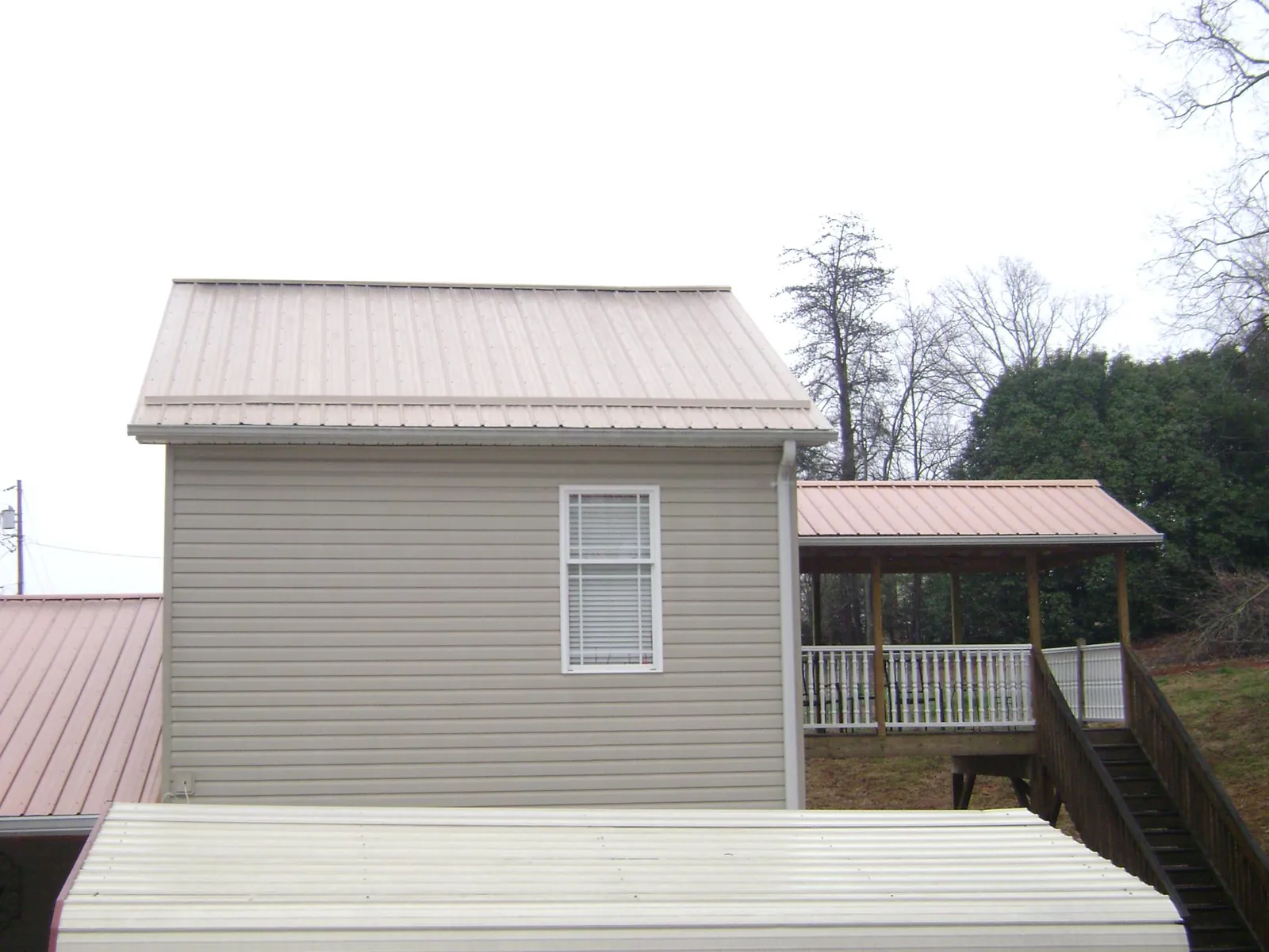 Tan metal roofs on a two story addition and attached porch, from a Roof Replacement job in Jeanerette